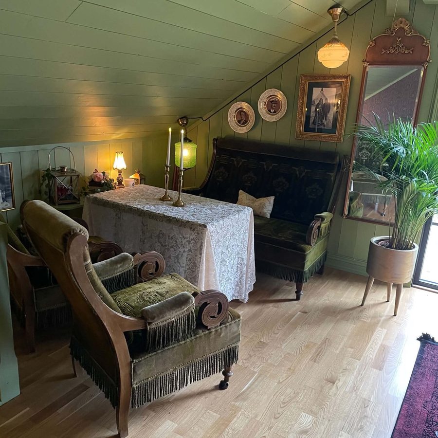 Salonghjørne i loftsstuen med grønne fløyelsmøbler, gammelt speil og bilder på veggen